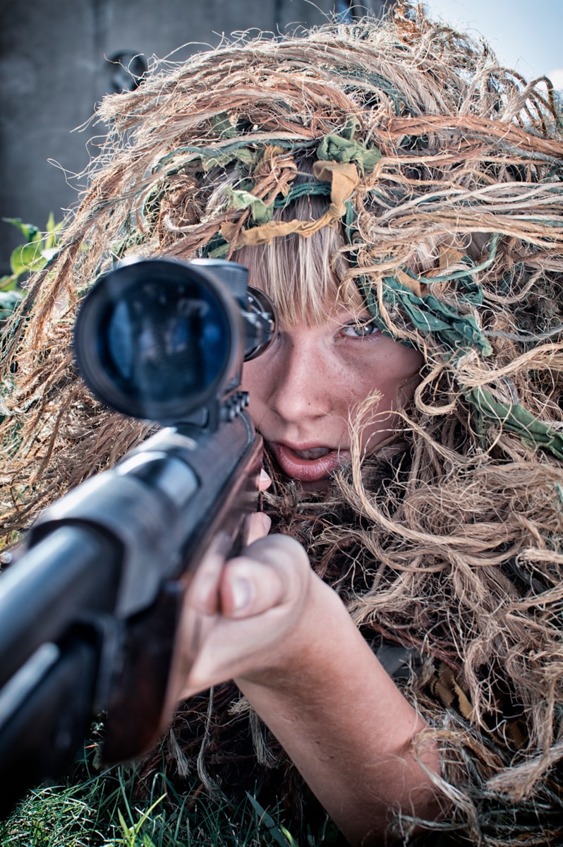 woman wearing gillie suit holding sniper rifle